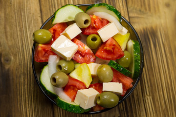 Greek salad in glass bowl on wooden table