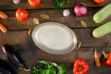 Around the vintage pan different vegetables on wooden table