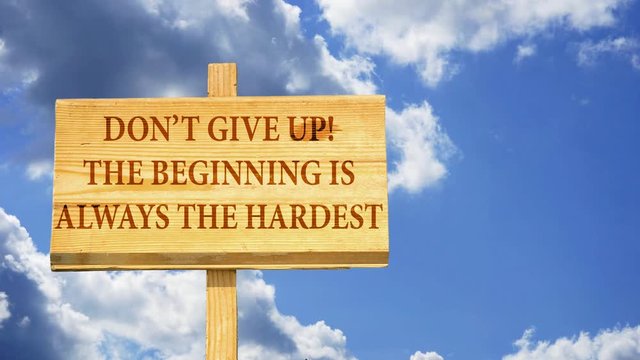 Don't give up. The beginning is always the hardest. Words on a wooden sign against time lapse clouds in the blue sky.
