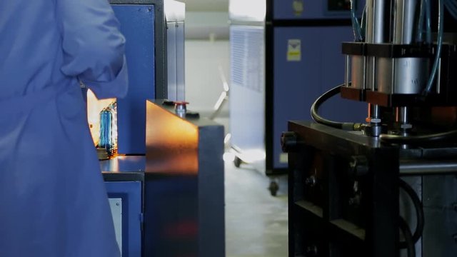 Employee of plant on a machine blows bottle preforms manufacturing plastic shapes. Female uniformed moves workpiece from one department to another machine
