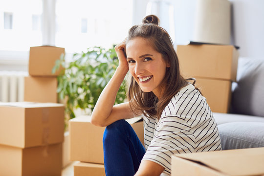 Young woman sitting in new apartment with cardboard boxes moving in