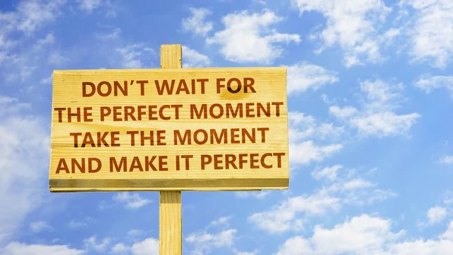 Don't wait for the perfect moment. Take the moment and make it perfect. Words on a wooden sign against time lapse clouds in the blue sky. 
