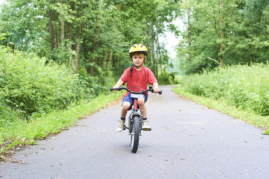 Child boy on a bicycle on bicycle path in summer. Boy cycling outdoors in safety helmet
