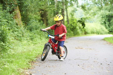 Child boy on a bicycle on bicycle path in summer. Boy cycling outdoors in safety helmet
