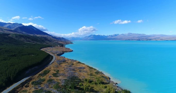 New Zealand aerial drone footage of lake Pukaki and southern alps on South Island. Road and clear blue lake and sky with Aoraki / Mount Cook National Park in background. New Zealand Tourist attraction