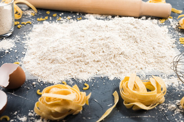 Raw homemade pasta on grey background. Fresh homemade pasta ingredients and rolling pin on the dark wooden table. Top view. Copy space