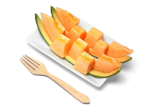 Sliced orange melon in pieces on a white plate with wooden fork.
