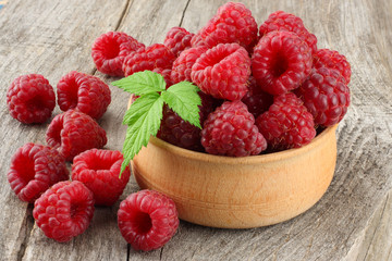 ripe raspberries in wooden bowl on old wooden table background