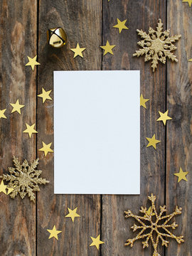 Mock up greeteng card on wood rustic background with Christmas decorations glitter snowflakes, bell and gold stars confetti. Invitation, paper. Place for text flat lay