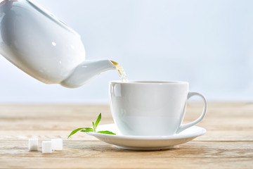 cup with green tea and teapot on white wooden table background