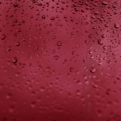 Drops of rain on red glass background. Natural Pattern of raindrops. Rain in the city.
