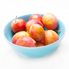 Ripe Pink Plums in a blue bowl, macro. Fresh plumps on rustic wooden table with copy space