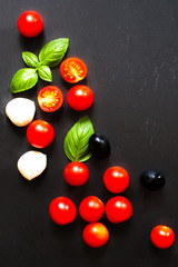 Fototapeta na wymiar Tomatoes, basil leaf, mozarella cheese and black olives. Fresh vegetables and fresh herbs over dark chalk board background. Food ingredients