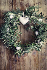 Corona navideña con ramas de olivo y adornos blancos sobre fondo de madera envejecida