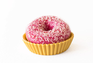 Brightly pink donut on a white background in a yellow ceramic holder
