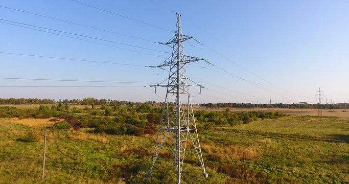 AERIAL: Flying up the high voltage electricity tower and power lines, above the beautiful agricultural field