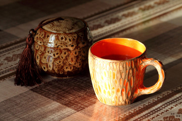 Orange ceramic handmade cup with tea on the table in the rays of the setting sun