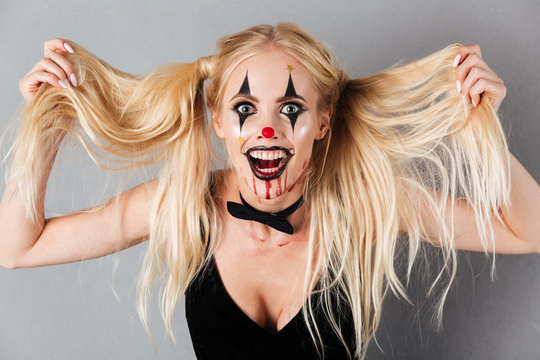 Playful blonde woman in halloween make up holding her hair