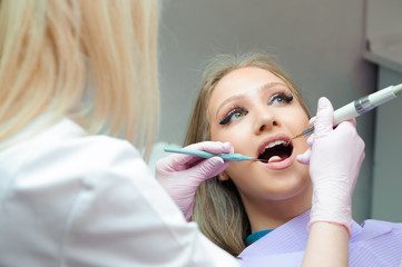 Doctor in uniform checking up female patient's teeth in dental clinic