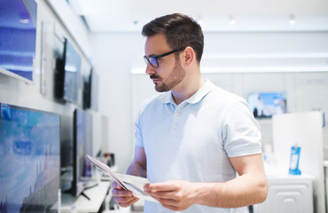 Fototapeta premium Man at tech store shopping new TV. Looking for a new big screen. Shopping time.