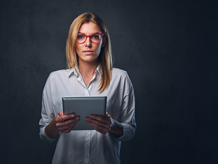 A blond female holds tablet PC on grey background.