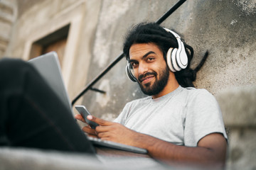 Casual young hipster with dreadlocks listening music holding mobile phone.