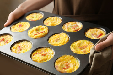Woman holding baking mold with tasty egg muffins, closeup