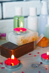 SPA procedures. Multicolored pieces of soap with candles, wax and bath salt. Bathroom accessories in a bright room with white brick.