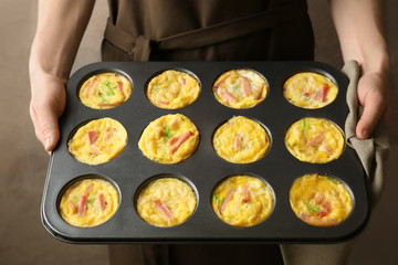 Woman holding baking mold with tasty egg muffins, closeup