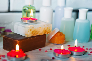 Obraz na płótnie Canvas SPA procedures. Multicolored pieces of soap with candles, wax and bath salt. Bathroom accessories in a bright room with white brick.