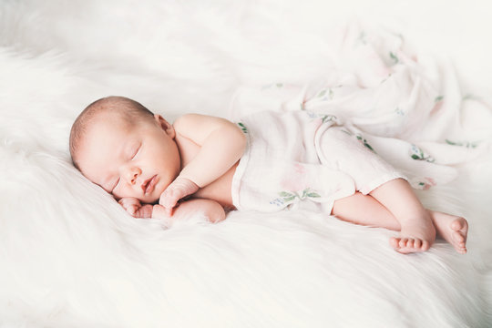 Sleeping newborn baby in a wrap on white blanket.