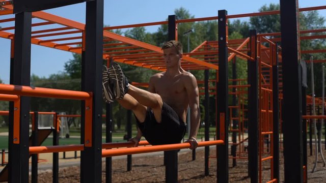 Topless athlete performing abdominal exercises on the parallel bars.