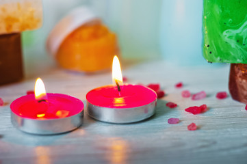 Obraz na płótnie Canvas SPA procedures. Multicolored pieces of soap with candles, wax and bath salt. Bathroom accessories in a bright room with white brick.