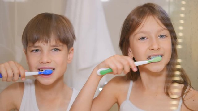 Children brush their teeth. A boy and a girl brush their teeth in the bathroom. The children clean their teeth.