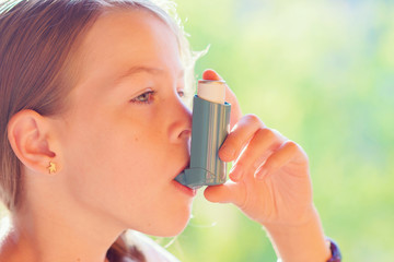 Girl using asthma inhaler in a park - obrazy, fototapety, plakaty