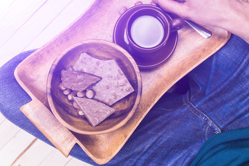 A man sits on the wooden floor, drinking coffee with chocolate. Close-up.