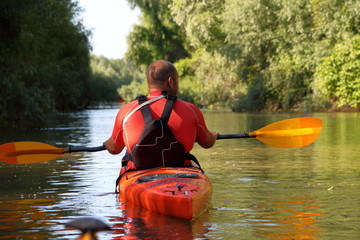 Man paddling in a red kayak and black life jacket kayaking in wild Danube river on biosphere reserve in spring