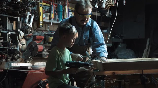 Adult carpenter man and grandson make a product from wood and screws with a screwdriver.