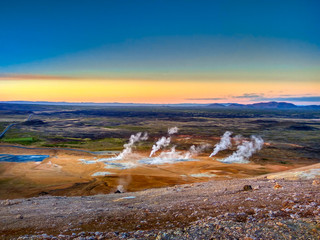 Mountain valley with several smoking geysers, at sunset