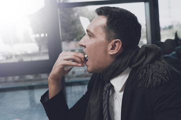 A sick man is sitting at his workplace in the office. He sprays himself in the throat of a medical spray