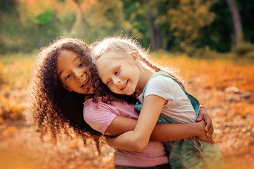 Two happy girls as friends hug each other in cheerful way. Little girlfriends in park.