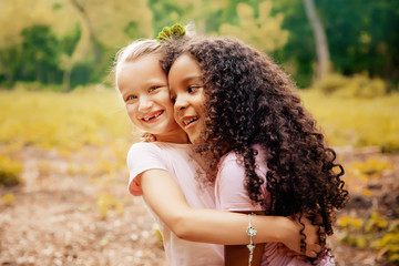 Two happy girls as friends hug each other in cheerful way. Little girlfriends in park.
