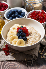 homemade oatmeal with berries on wooden background, vertical