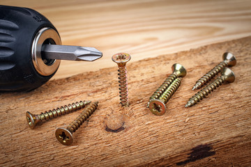cordless drill and large screws on a wood background - obrazy, fototapety, plakaty
