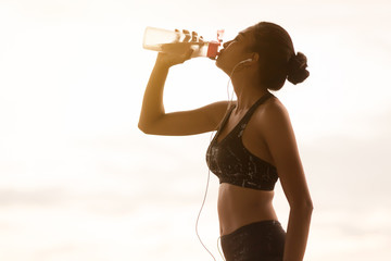 Asian young woman drinking water sunny evening 
 after jogging.