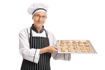 Elderly baker holding a tray with freshly baked cookies