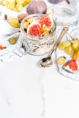 Autumn breakfast ideas, recipes. Jar of overnight autumn oats with red figs, grapes and walnuts. On white marble table, copy space