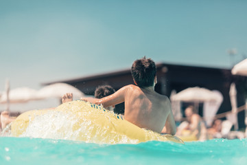 Young people on the water slide in the aqua fun park having fun on the glides, they are happy and...