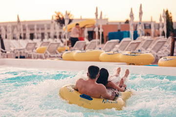 Couple having fun on the water slide in the aqua fun park glides, they are happy and water splashes...