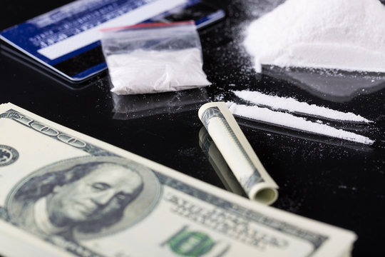 Rolled hundred dollars banknote, two lines and plastic packet of cocaine